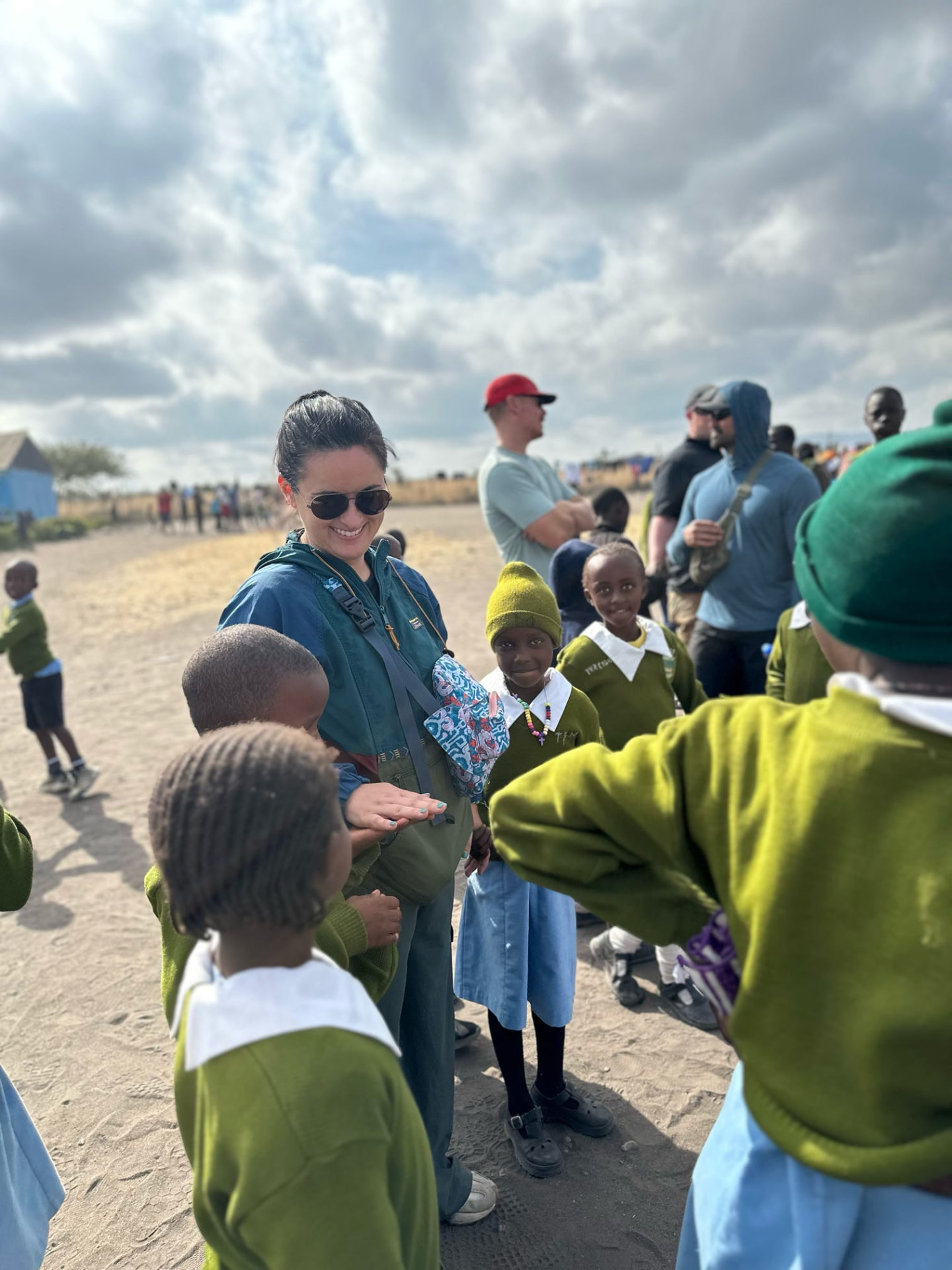 A team member playing a clapping game with students on a dusty field