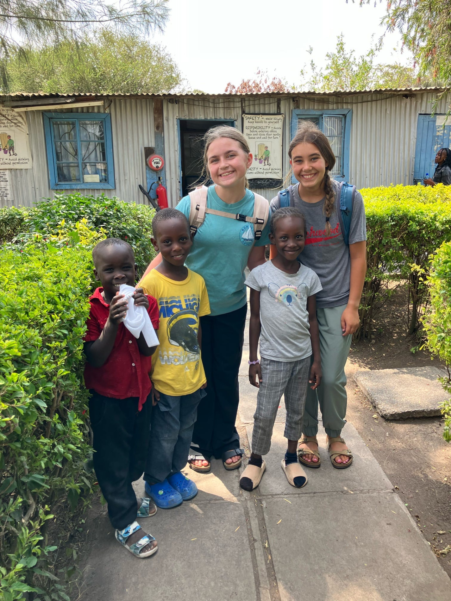 Two team members standing with four Kenyan children outside a corrugated iron school
