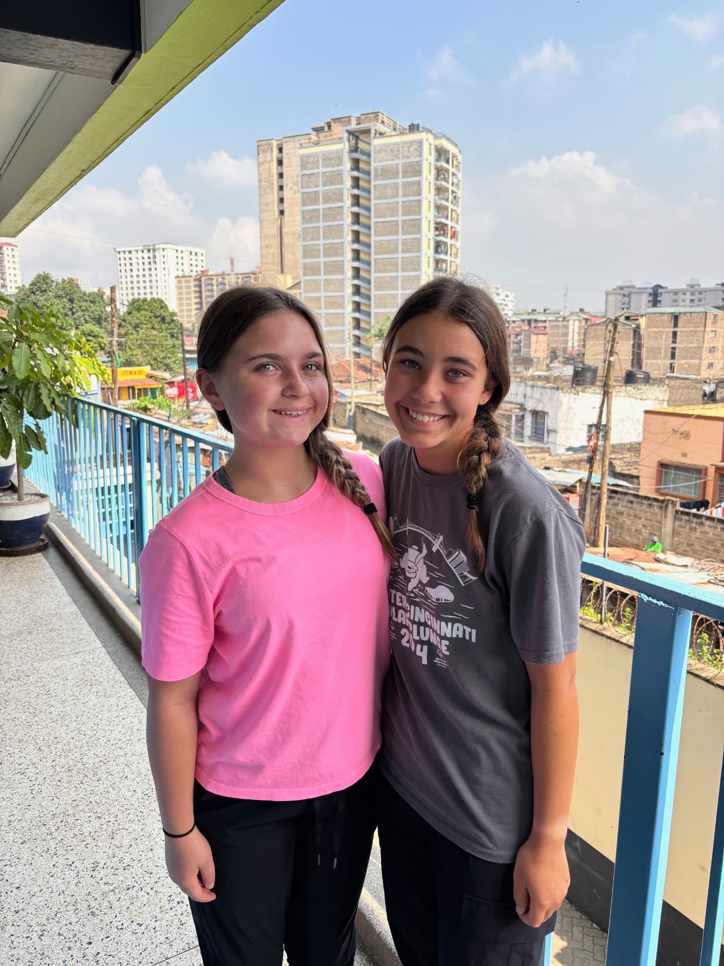 Two teenage girls smiling on a balcony overlooking Nairobi