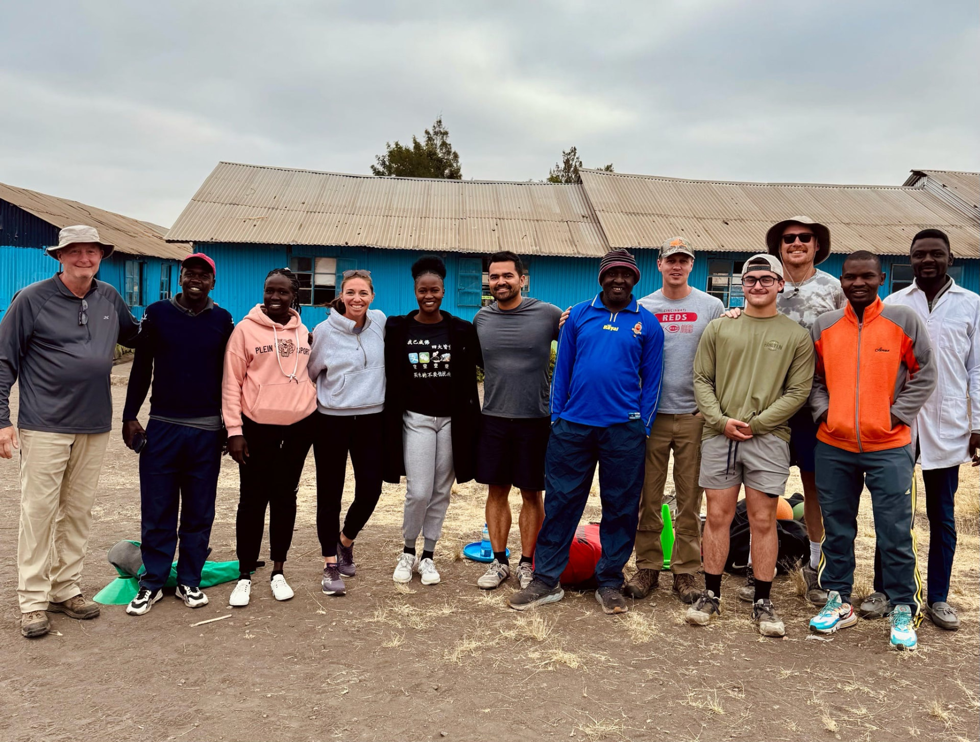 The full team with Kenyan staff standing together in front of a blue school building