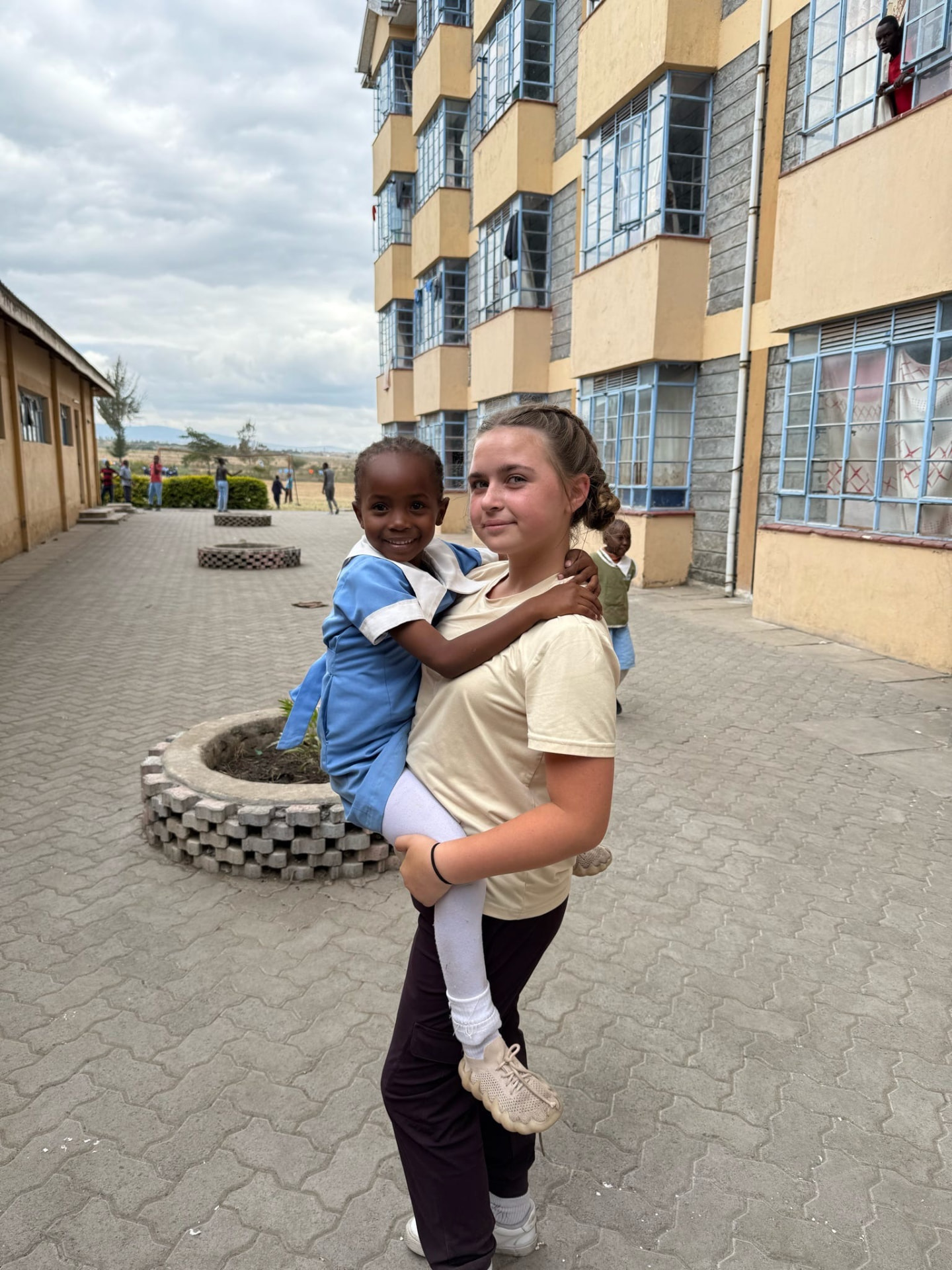 A team member carrying a young student in a blue uniform in the school courtyard
