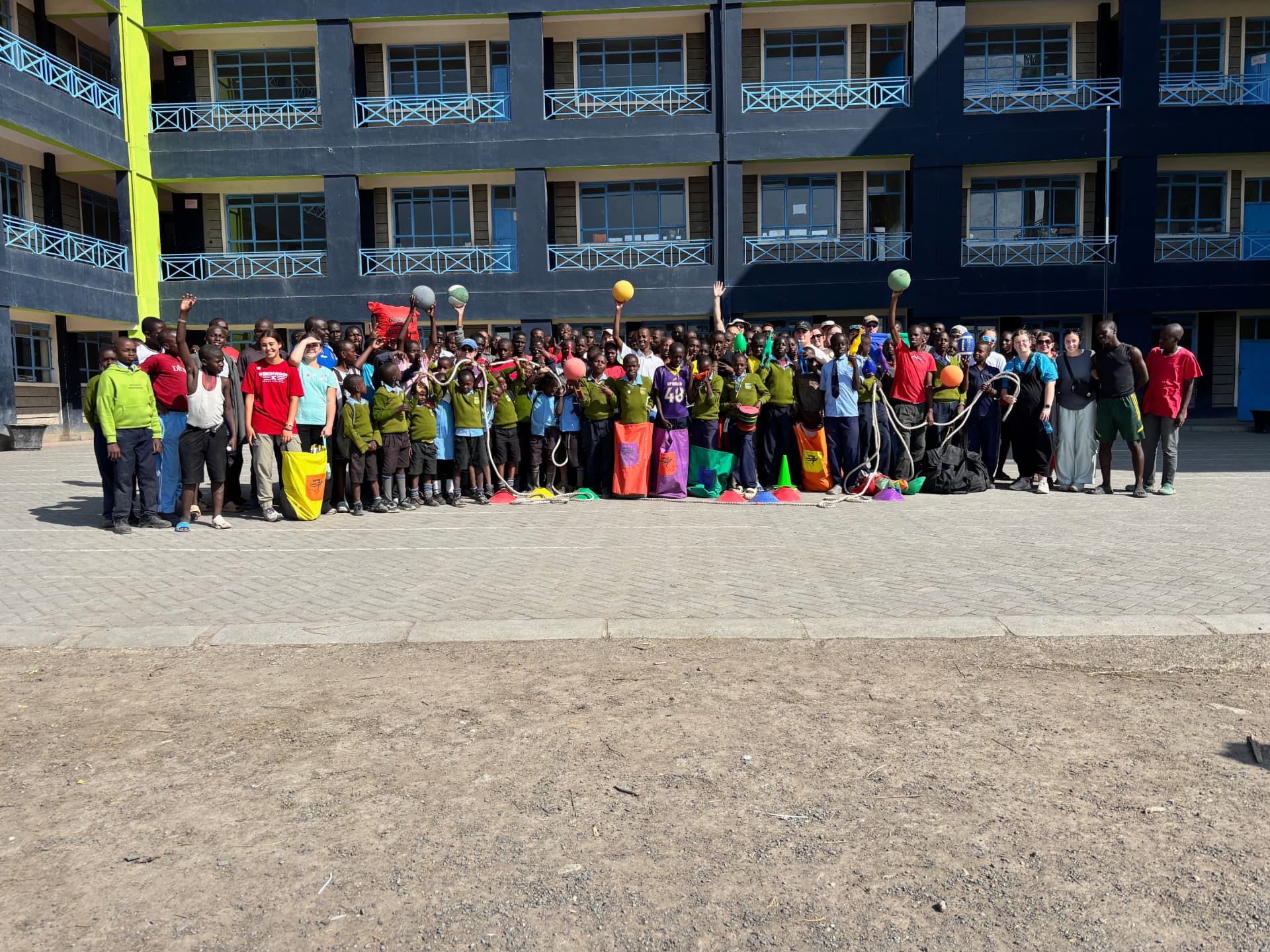 Large group of students and team members gathered with sports equipment in the school courtyard