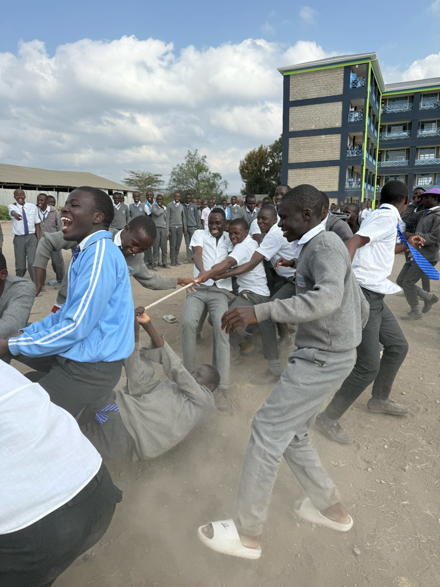 Secondary students laughing during a tug-of-war on the school field